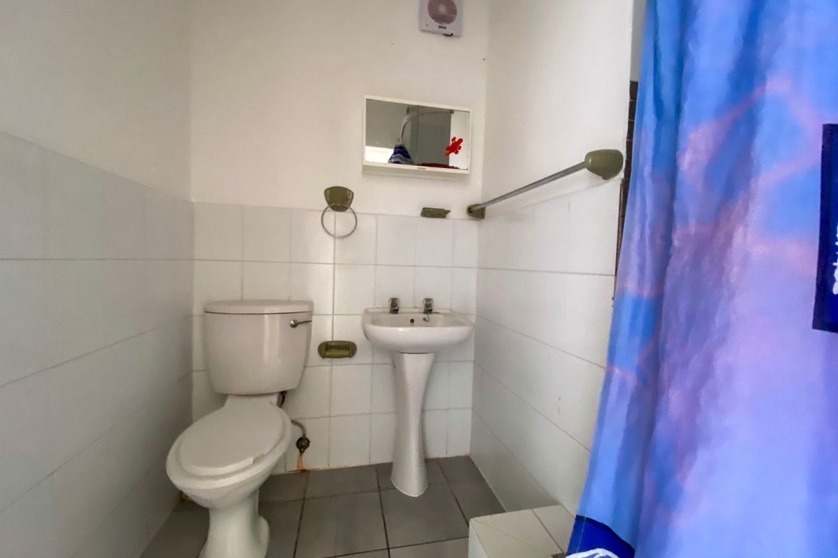 A compact bathroom featuring a pedestal basin, toilet, and wall-to-floor tiling, requiring cosmetic updates to improve its overall condition and appeal.