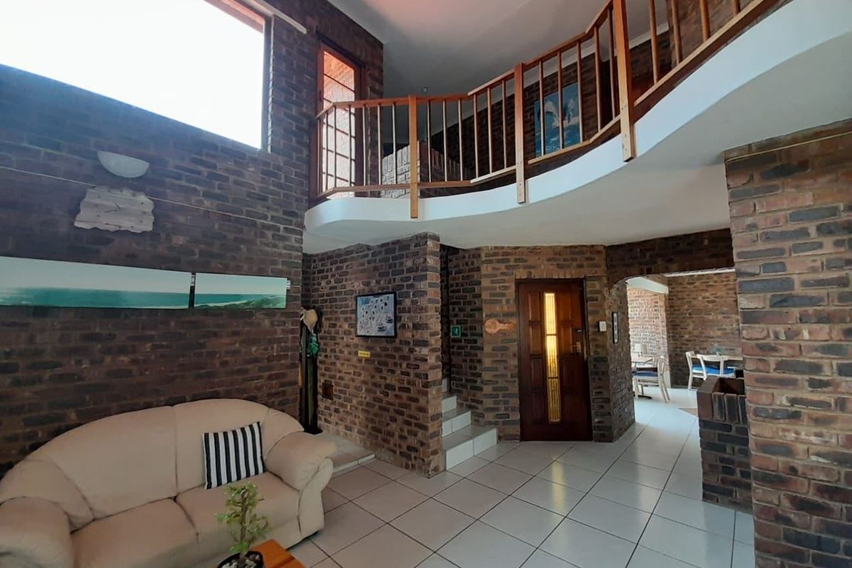 Spacious living area featuring double-volume ceilings, exposed brick walls, and a mezzanine level with a wooden balustrade, creating an open and airy atmosphere.
