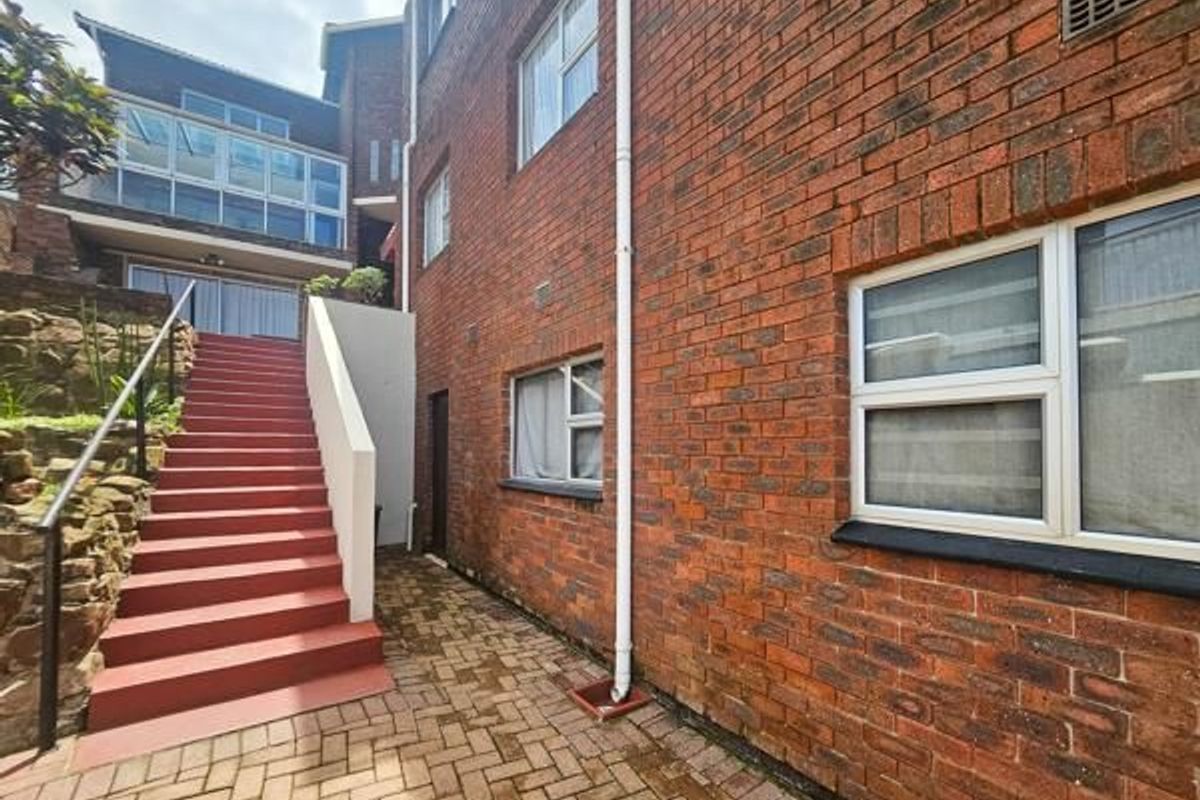 Rear exterior view of the property featuring a red brick facade, paved courtyard area, and an external staircase leading to the upper level.