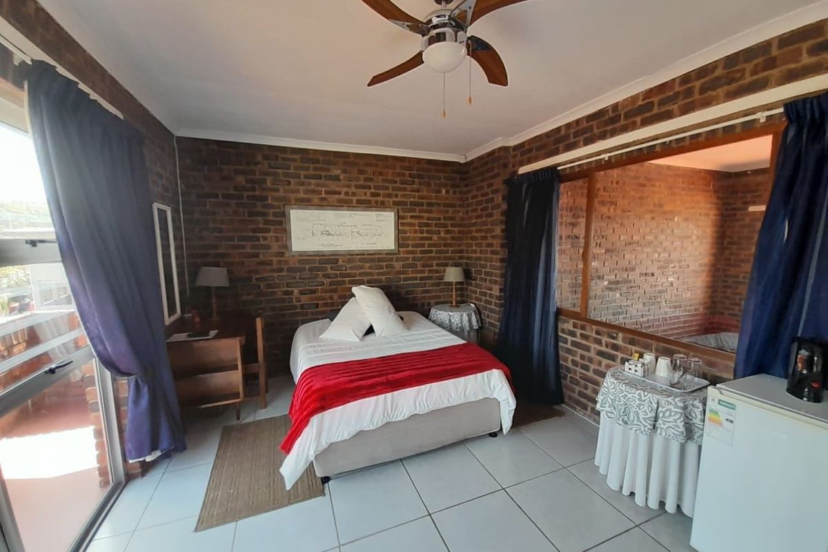 A bedroom featuring exposed brick walls, tiled flooring, a ceiling fan, and a sliding glass door providing access to an outdoor area.
