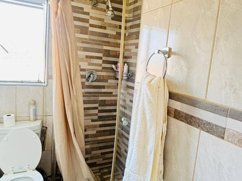 A functional bathroom featuring a corner shower enclosure, tiled walls, and a standard toilet suite.