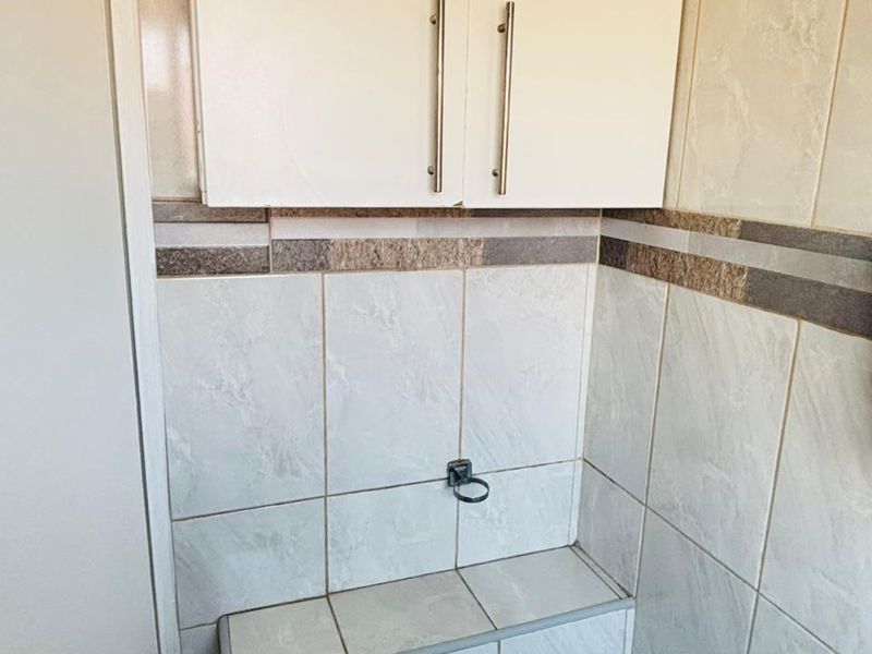 A compact bathroom area featuring tiled walls, a built-in tiled ledge, and a white wall-mounted storage cabinet.