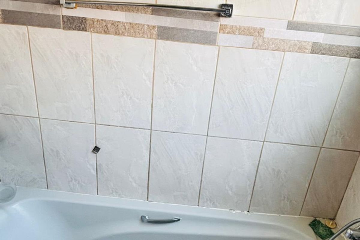 A functional bathroom featuring a standard bathtub with a handheld shower attachment and neutral ceramic wall tiling.