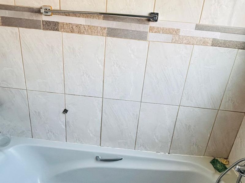 A functional bathroom featuring a standard bathtub with a handheld shower attachment and neutral ceramic wall tiling.