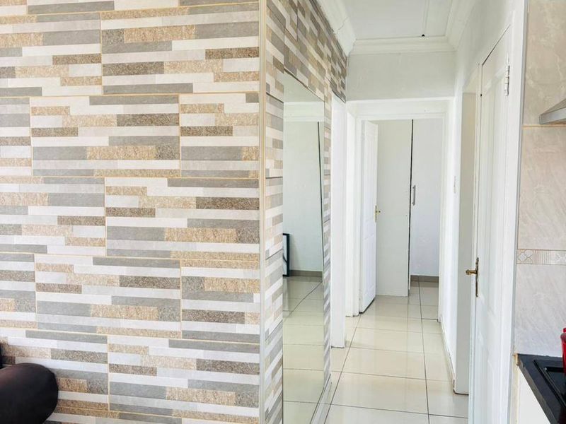 A bright hallway featuring neutral floor tiles, decorative textured wall tiling, and a built-in mirror, leading to multiple interior rooms.