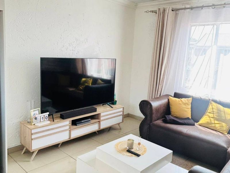 A bright living room featuring tiled flooring, textured walls, and window security bars, providing a functional and comfortable space.