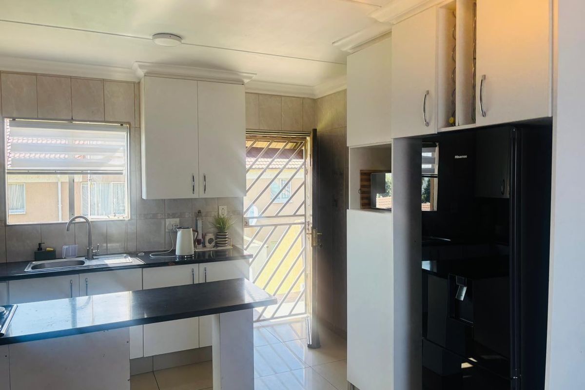 Functional kitchen featuring white cabinetry, dark countertops, tiled backsplash, and direct access to the exterior via a security gate.