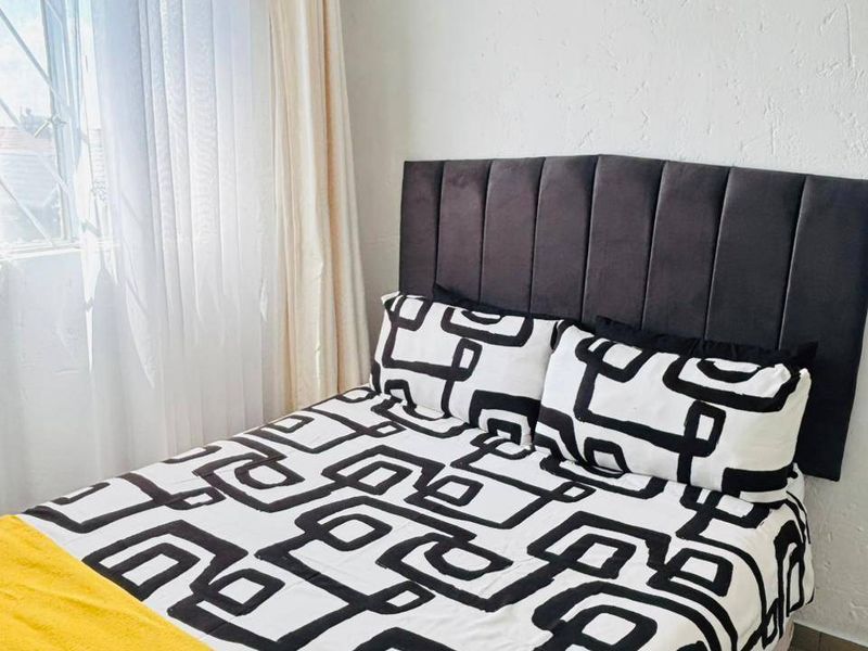 A cozy bedroom featuring tiled flooring and a window fitted with security bars, providing natural light.
