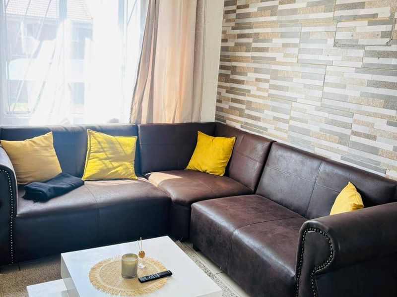 A comfortable living room featuring tiled flooring, a textured stone-look feature wall, and a large window allowing for natural light.
