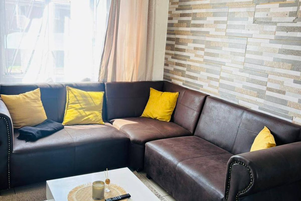 A comfortable living room featuring tiled flooring, a textured stone-look feature wall, and a large window allowing for natural light.