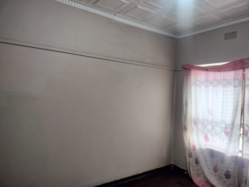 An empty bedroom featuring decorative ceiling tiles, a picture rail, and a window with security grilles.
