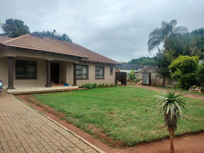 Front view of a single-story house featuring a tiled roof with solar water heater, covered porch, and a paved driveway leading to a lawn.