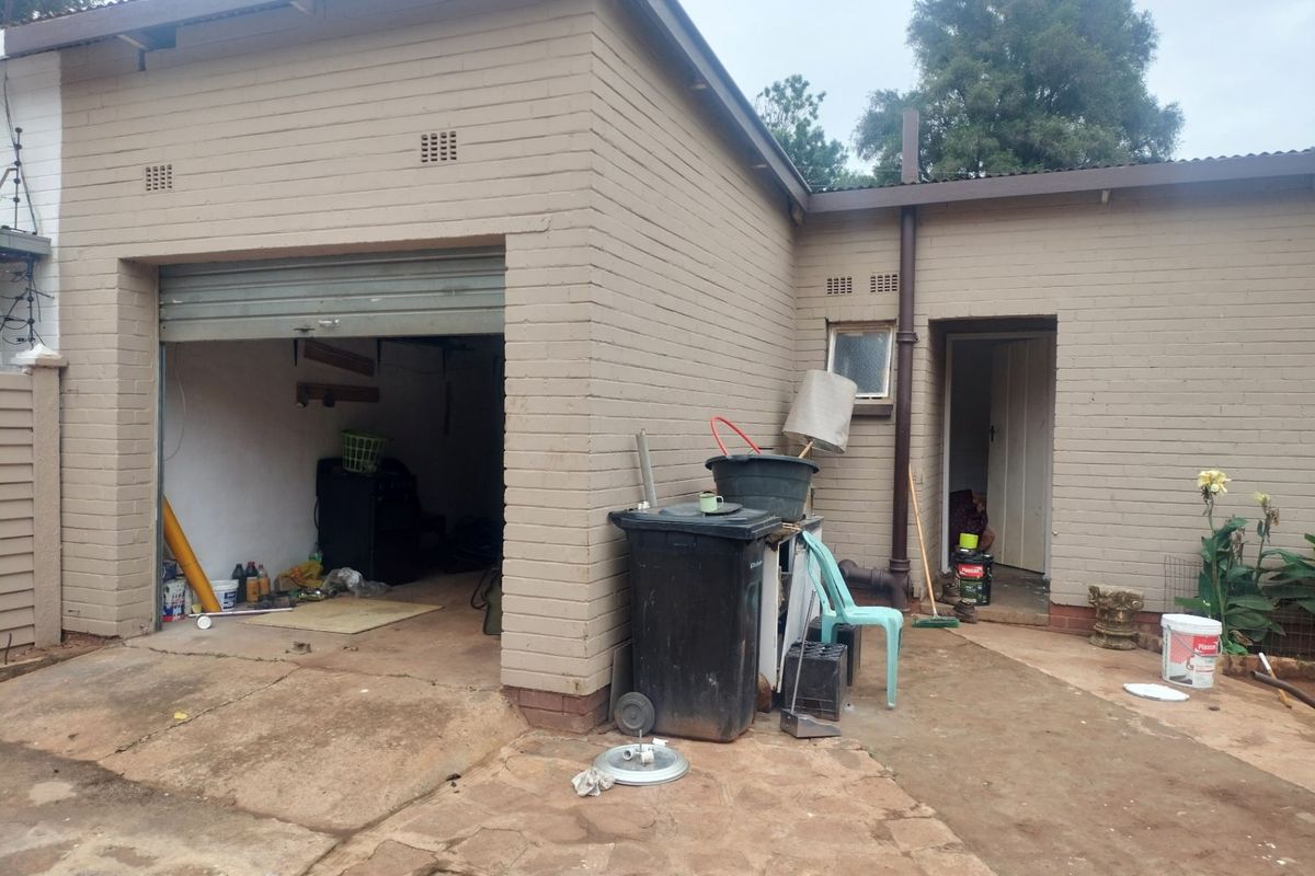Rear view of the property showing a single garage, brick exterior walls, and concrete paving in need of maintenance.
