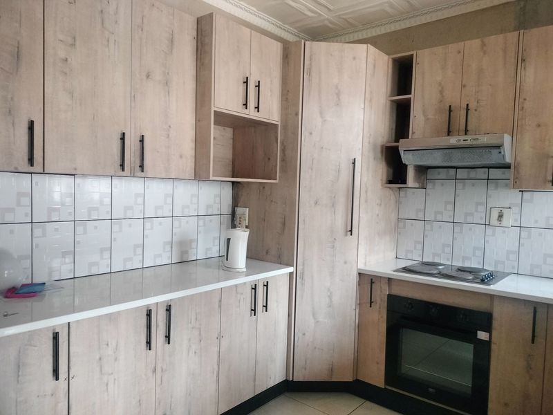 Modern kitchen featuring light wood-grain cabinetry, white countertops, tiled backsplash, and integrated appliances including an oven, hob, and extractor fan.