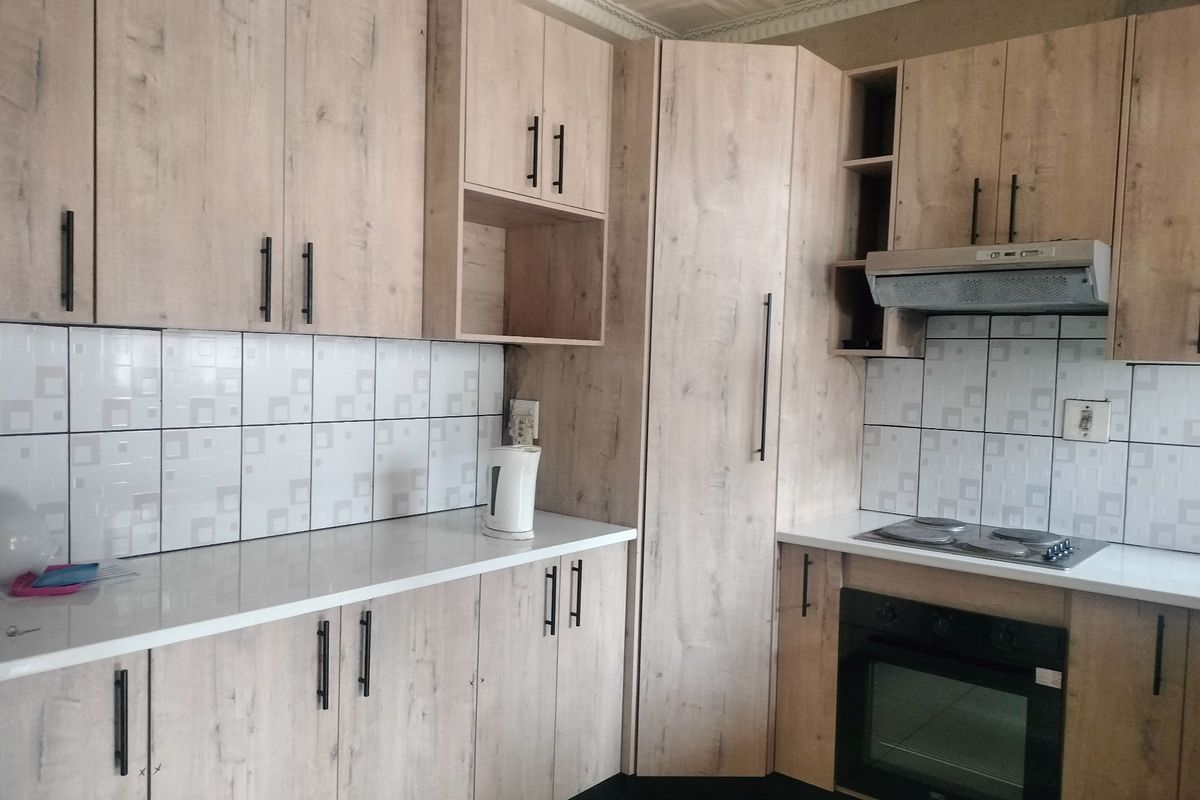 Modern kitchen featuring light wood-grain cabinetry, white countertops, tiled backsplash, and integrated appliances including an oven, hob, and extractor fan.