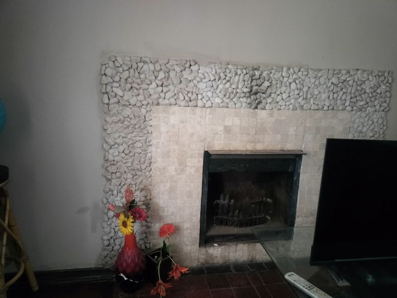 A living room featuring a fireplace with a stone-clad surround and tiled hearth, presenting an opportunity for modern cosmetic updates.