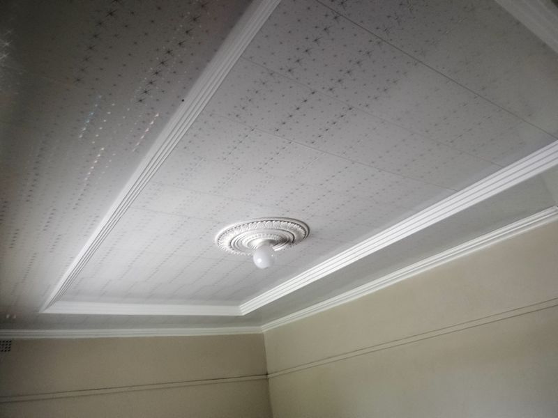 A view of a room ceiling featuring a decorative ceiling rose, coved cornicing, and patterned ceiling tiles.
