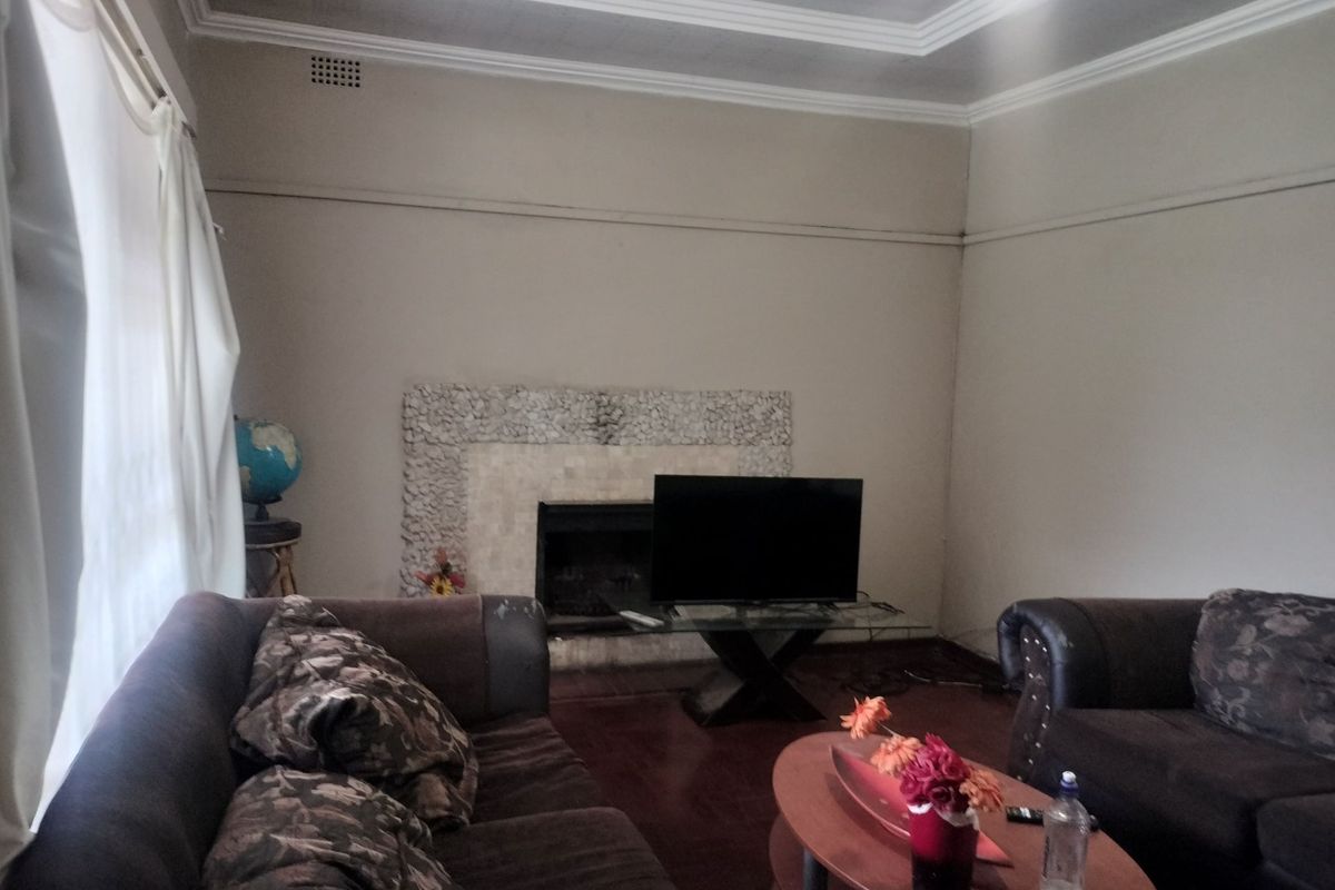 A living room featuring a stone-surround fireplace, coved ceilings, and hardwood flooring, offering a classic layout with potential for modernization.