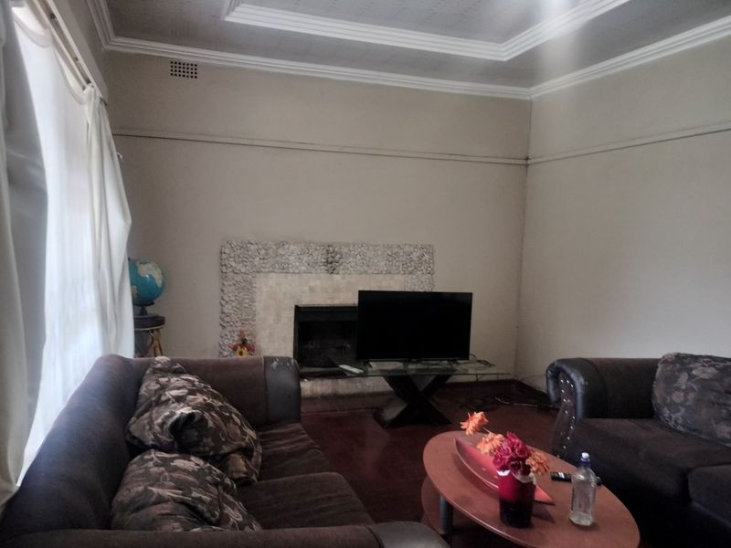 A living room featuring a stone-surround fireplace, coved ceilings, and hardwood flooring, offering a classic layout with potential for modernization.