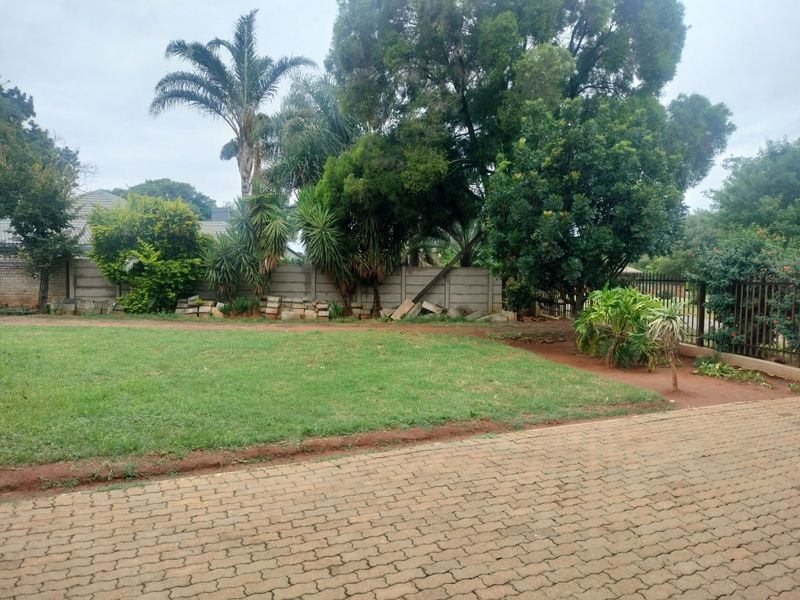 A spacious garden area featuring a paved driveway, mature trees, and a precast concrete boundary wall requiring maintenance.