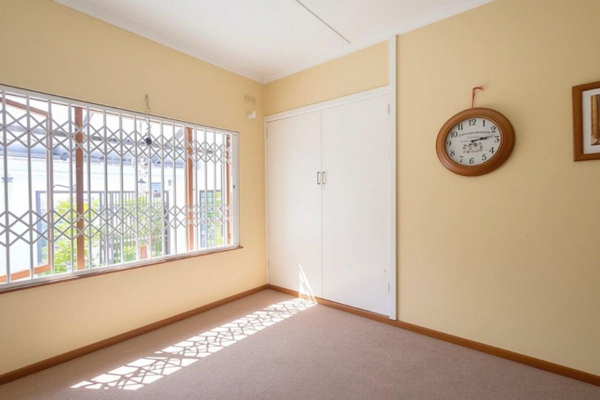 A bedroom featuring built-in cupboards, carpeted flooring, and a window fitted with security bars.