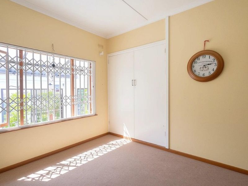 A bedroom featuring built-in cupboards, carpeted flooring, and a window fitted with security bars.