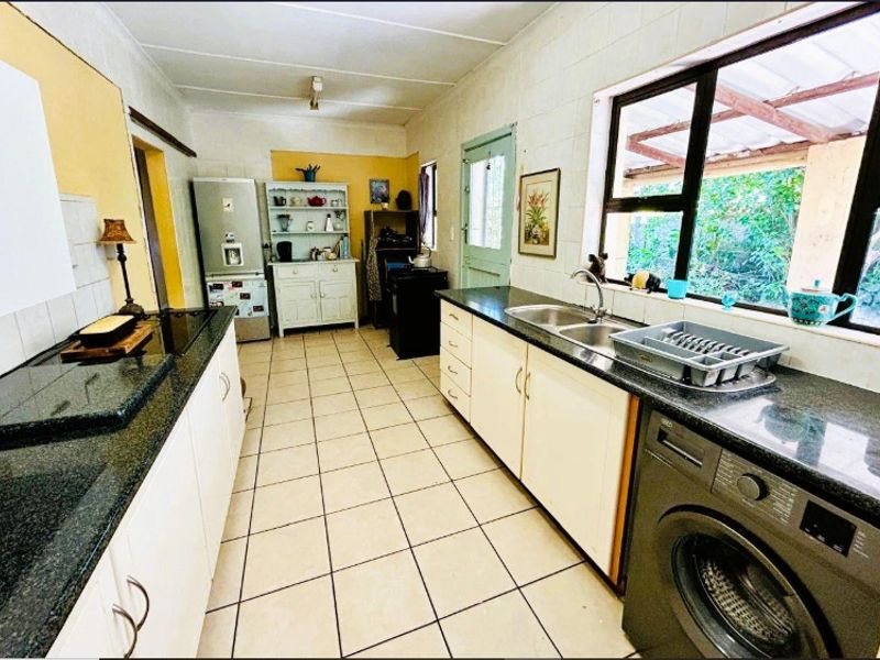 A functional kitchen featuring dark granite countertops, white cabinetry, a double sink, and tiled flooring with direct access to the exterior.