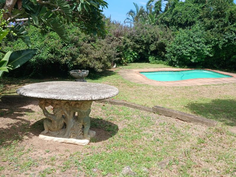 A private garden area featuring a swimming pool with brick coping, surrounded by mature landscaping and established trees.