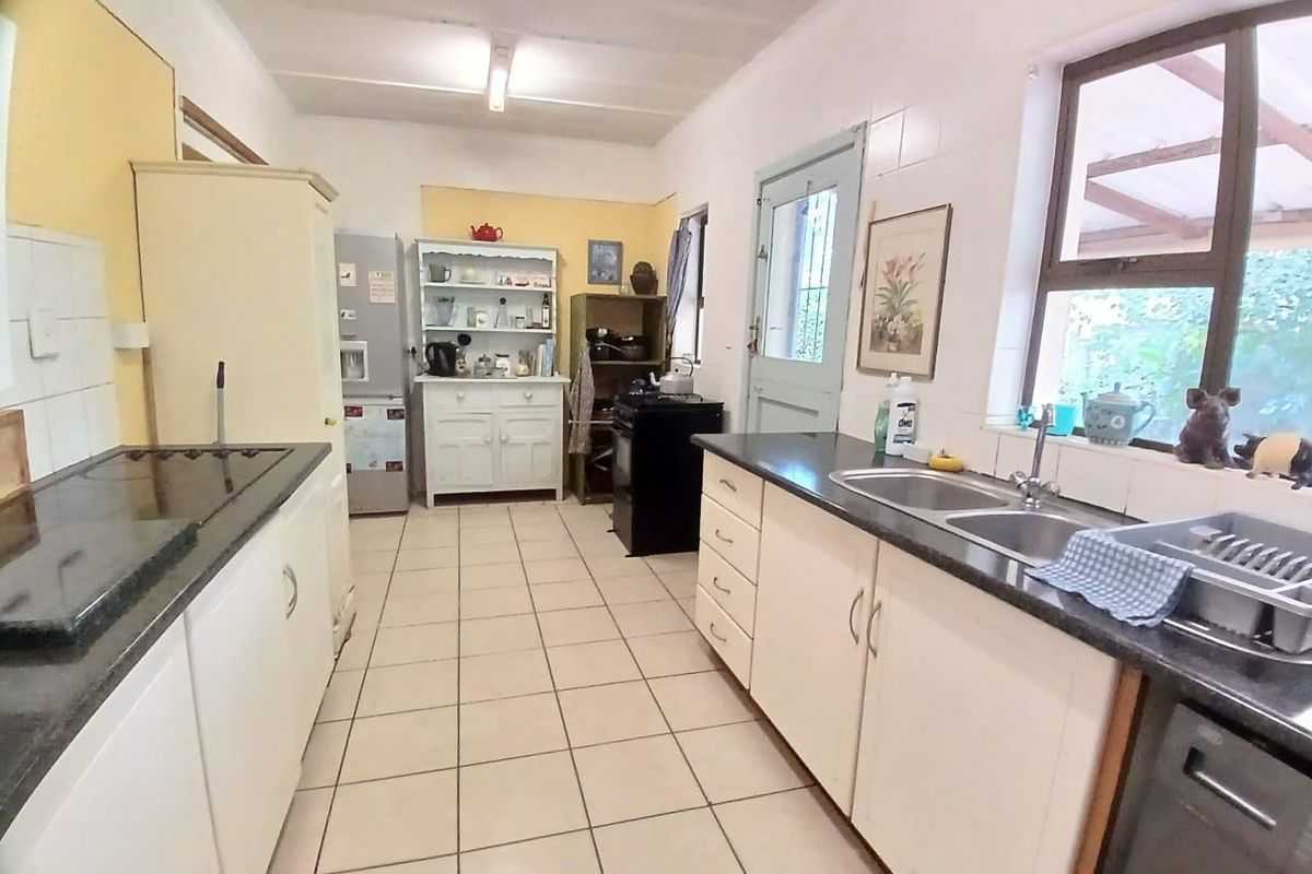 A functional kitchen featuring white cabinetry, dark countertops, a double-basin sink, and tiled flooring with direct access to the exterior.