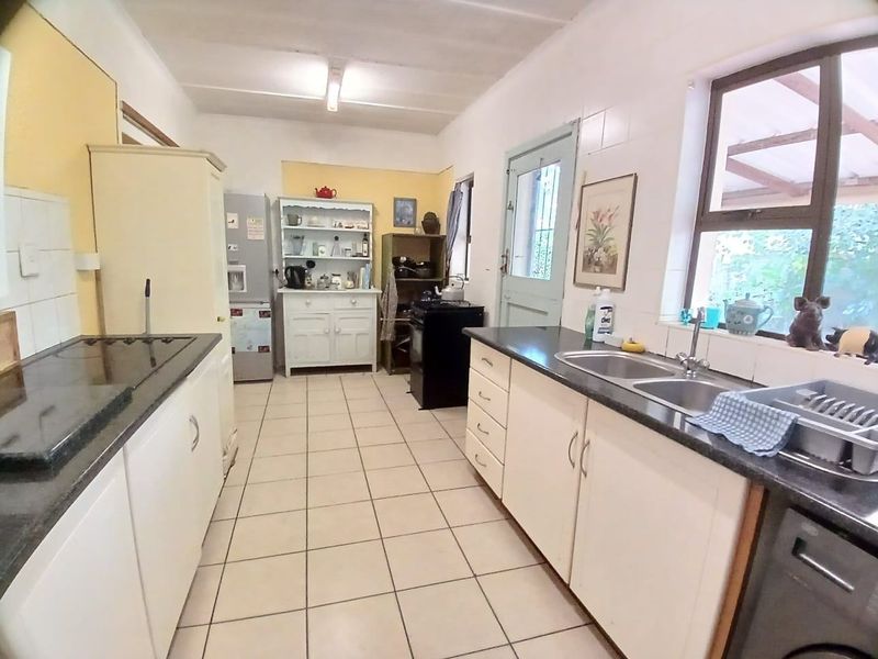 A functional kitchen featuring white cabinetry, dark countertops, a double-basin sink, and tiled flooring with direct access to the exterior.