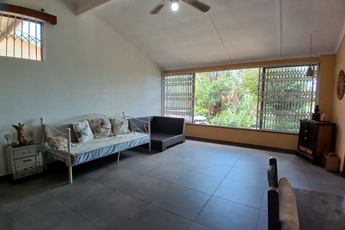 Spacious living room featuring large windows with security gates, vaulted ceilings with a fan, and neutral floor tiling.