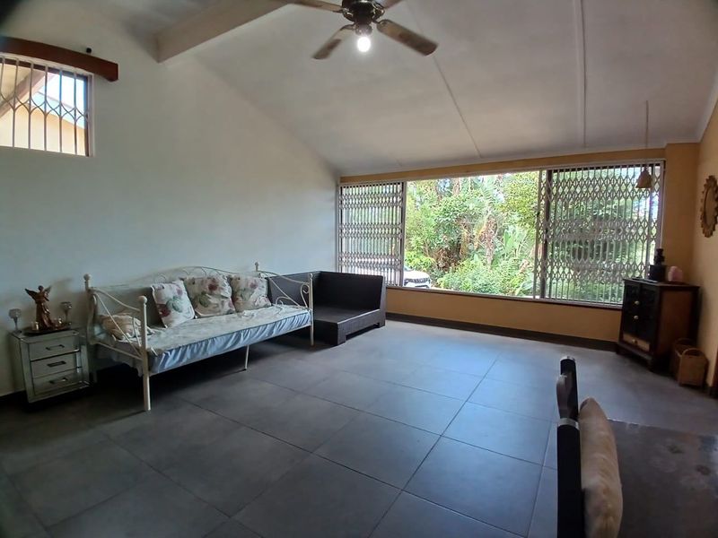 Spacious living room featuring large windows with security gates, vaulted ceilings with a fan, and neutral floor tiling.