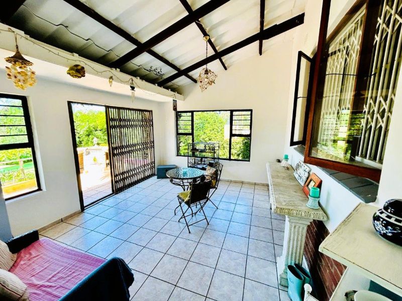 A bright, enclosed patio area featuring tiled flooring, exposed timber rafters, and large windows with security gates, offering a versatile indoor-outdoor living space.
