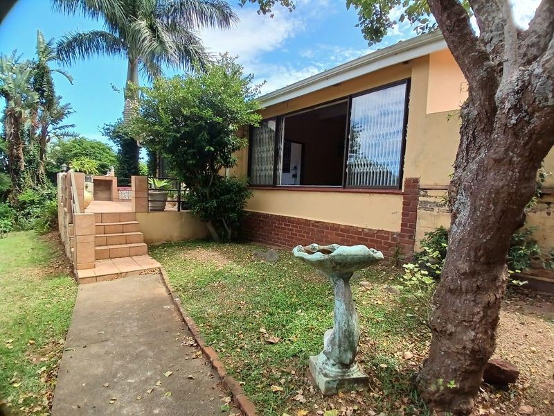 Rear exterior view featuring a paved patio area, garden space, and access to the home through large sliding windows.