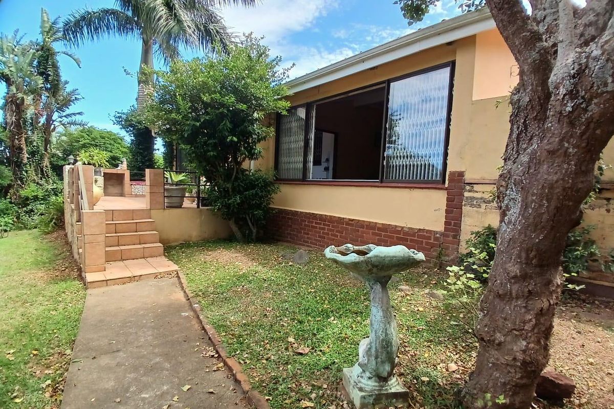Rear exterior view featuring a paved patio area, garden space, and access to the home through large sliding windows.