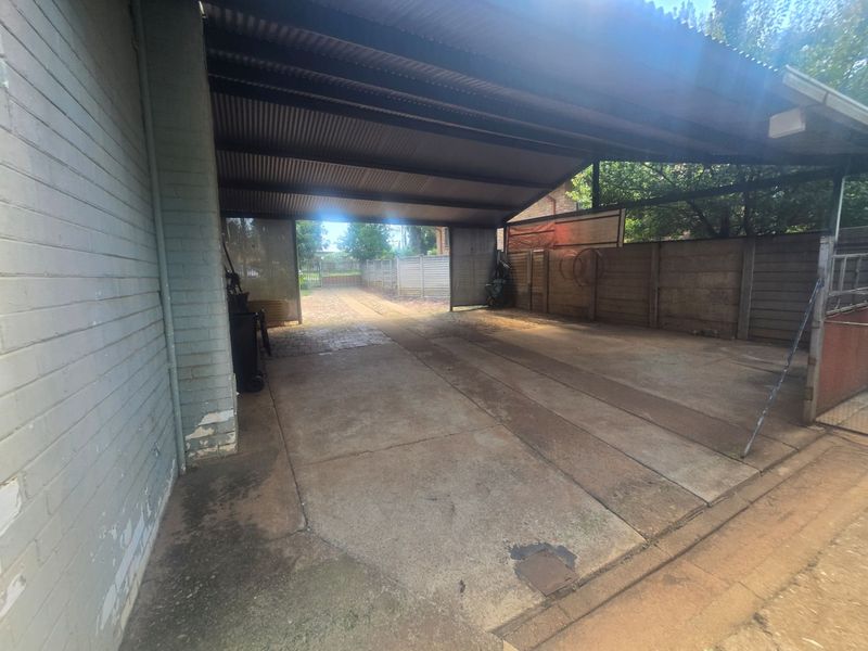A covered outdoor parking area or carport featuring a corrugated metal roof, concrete flooring, and perimeter walling.