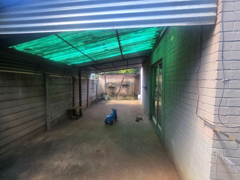 A covered outdoor patio area featuring a corrugated roof, concrete flooring, and direct access to the main dwelling via a sliding glass door.