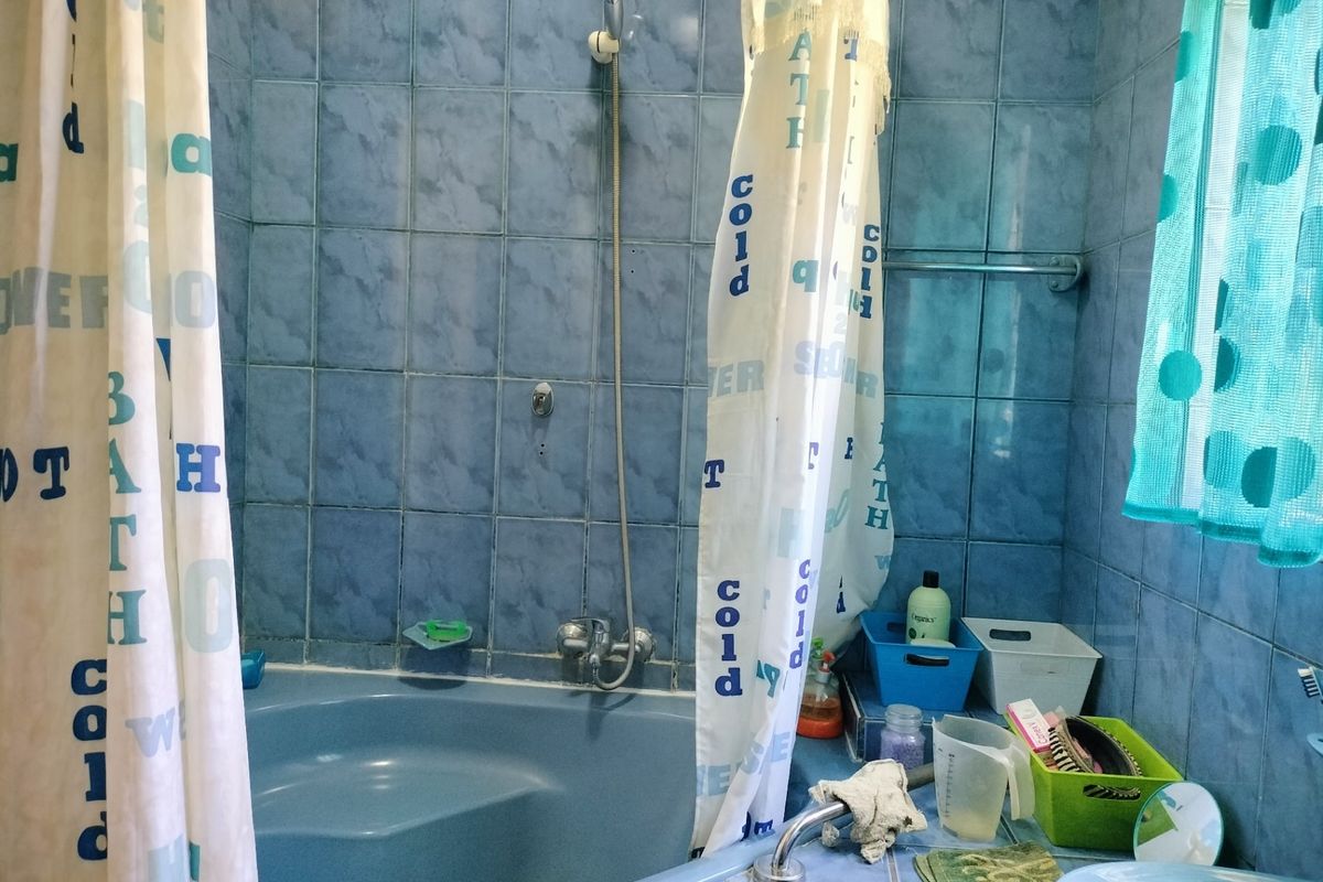 A dated bathroom featuring blue wall tiles, a built-in bathtub with shower mixer, and a vanity basin.