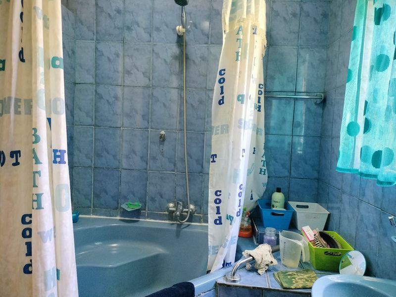 A dated bathroom featuring blue wall tiles, a built-in bathtub with shower mixer, and a vanity basin.