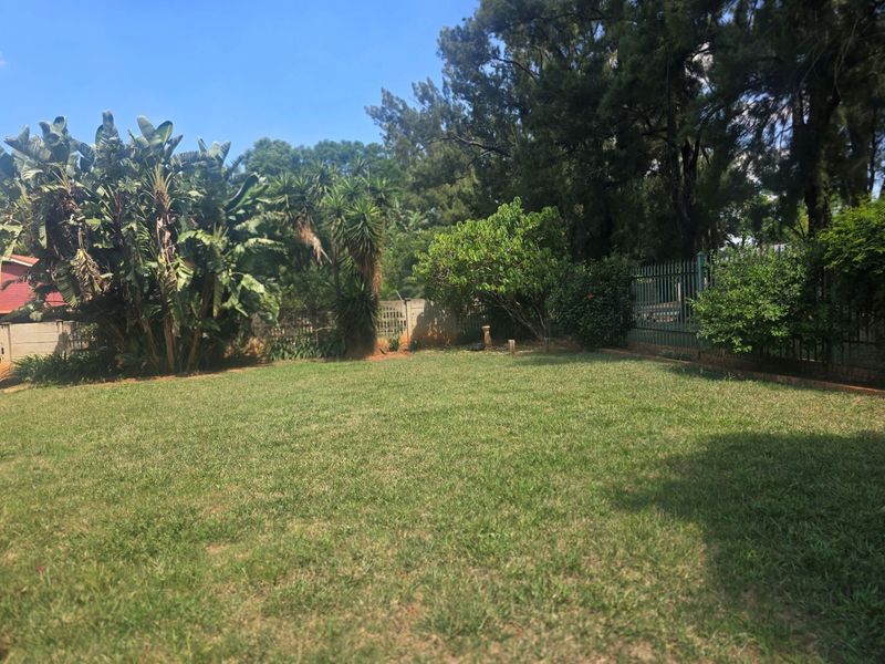A spacious, well-maintained private garden featuring a large lawn area, mature trees, and secure perimeter fencing.