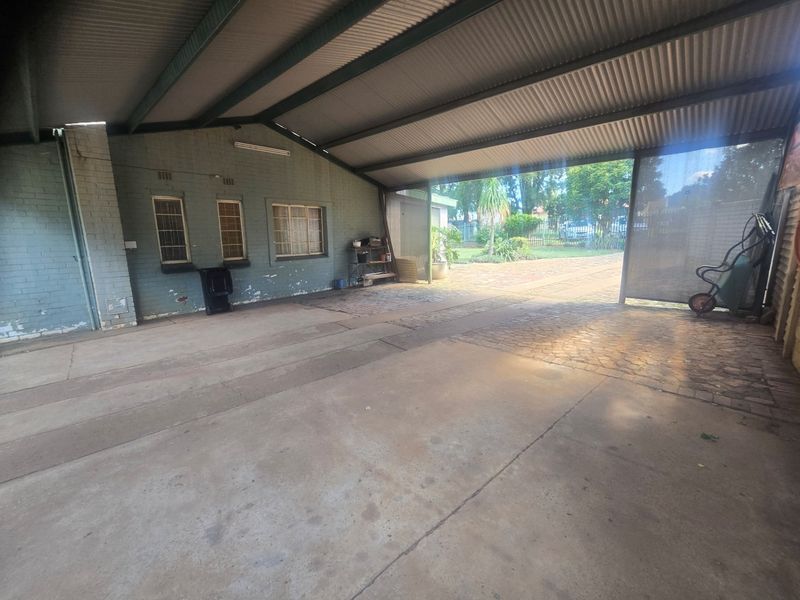 A spacious covered outdoor patio area featuring a corrugated metal roof, concrete flooring, and direct access to the rear garden.