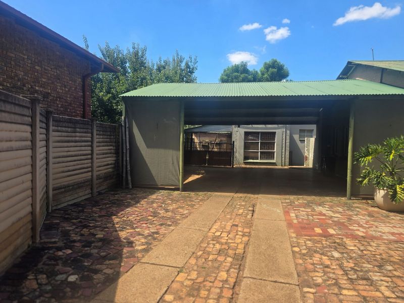A functional outdoor carport area featuring a corrugated metal roof and paved driveway, providing covered parking space alongside a precast concrete boundary wall.
