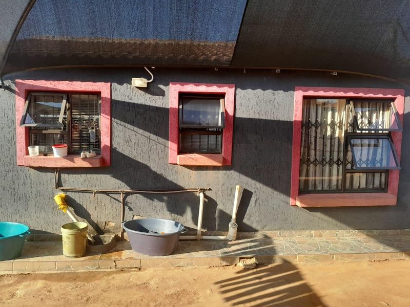 Rear exterior view of the house featuring a tiled patio area, security bars on windows, and external plumbing fixtures under a shade cloth canopy.