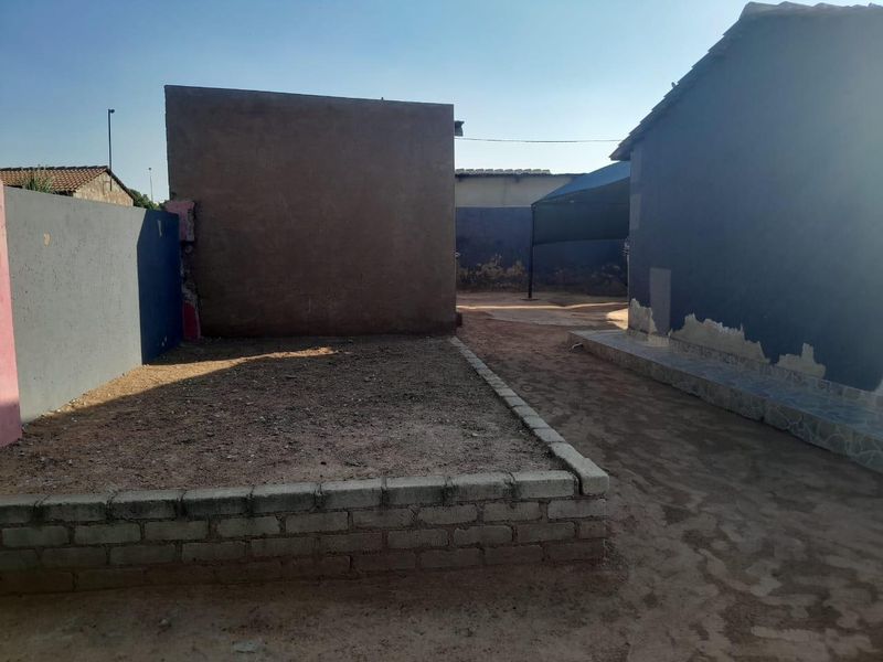 Rear exterior area featuring a raised brick planter, masonry boundary walls, and a tiled plinth, requiring maintenance and landscaping improvements.