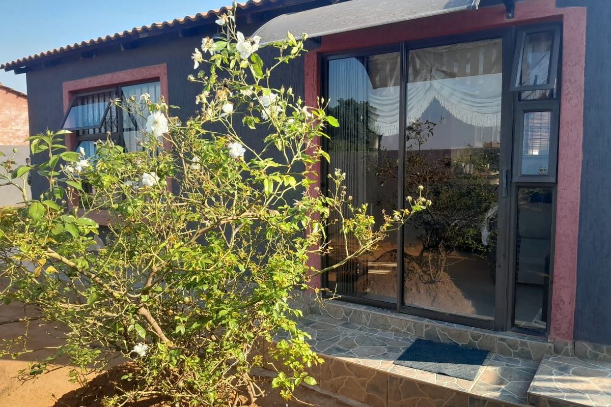 Rear exterior view of the property featuring a tiled patio area, sliding glass doors, and a protective awning over the entrance.