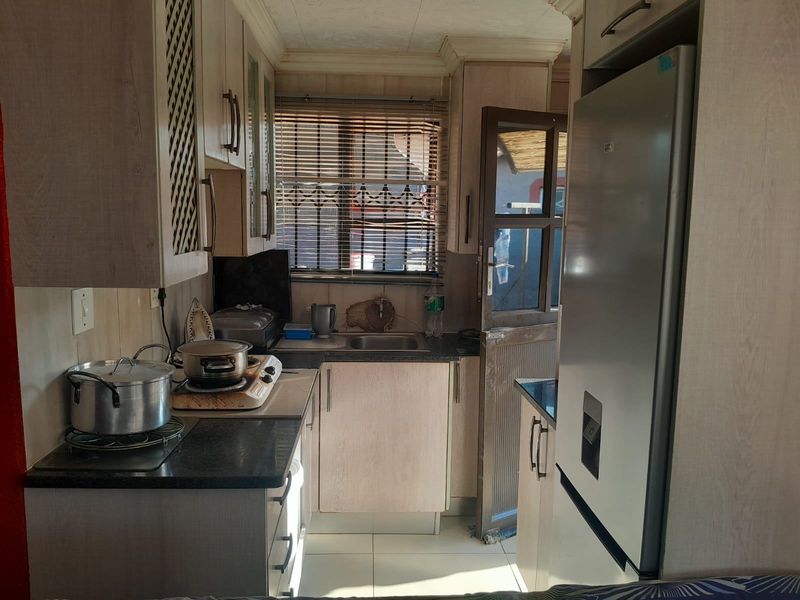 A compact kitchen featuring laminate cabinetry, granite countertops, and tiled flooring, with direct access to the exterior via a security door.