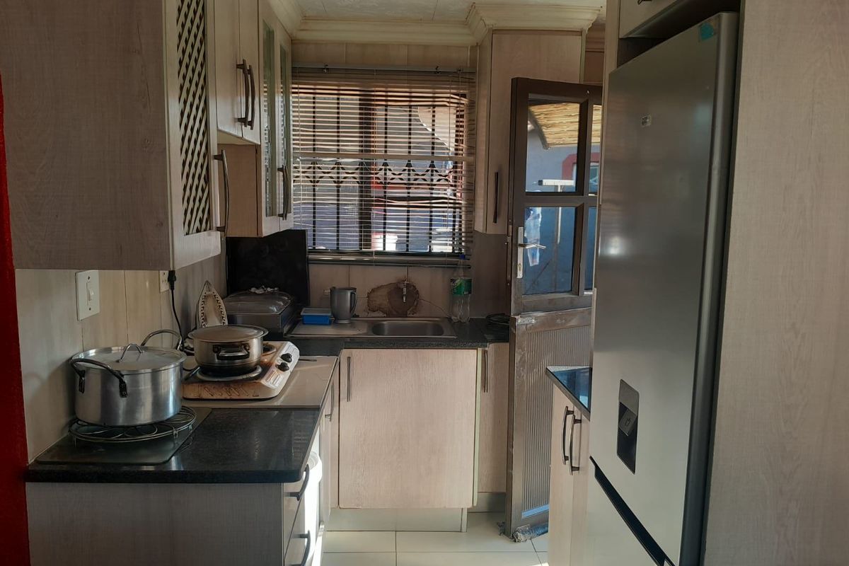 A compact kitchen featuring laminate cabinetry, granite countertops, and tiled flooring, with direct access to the exterior via a security door.