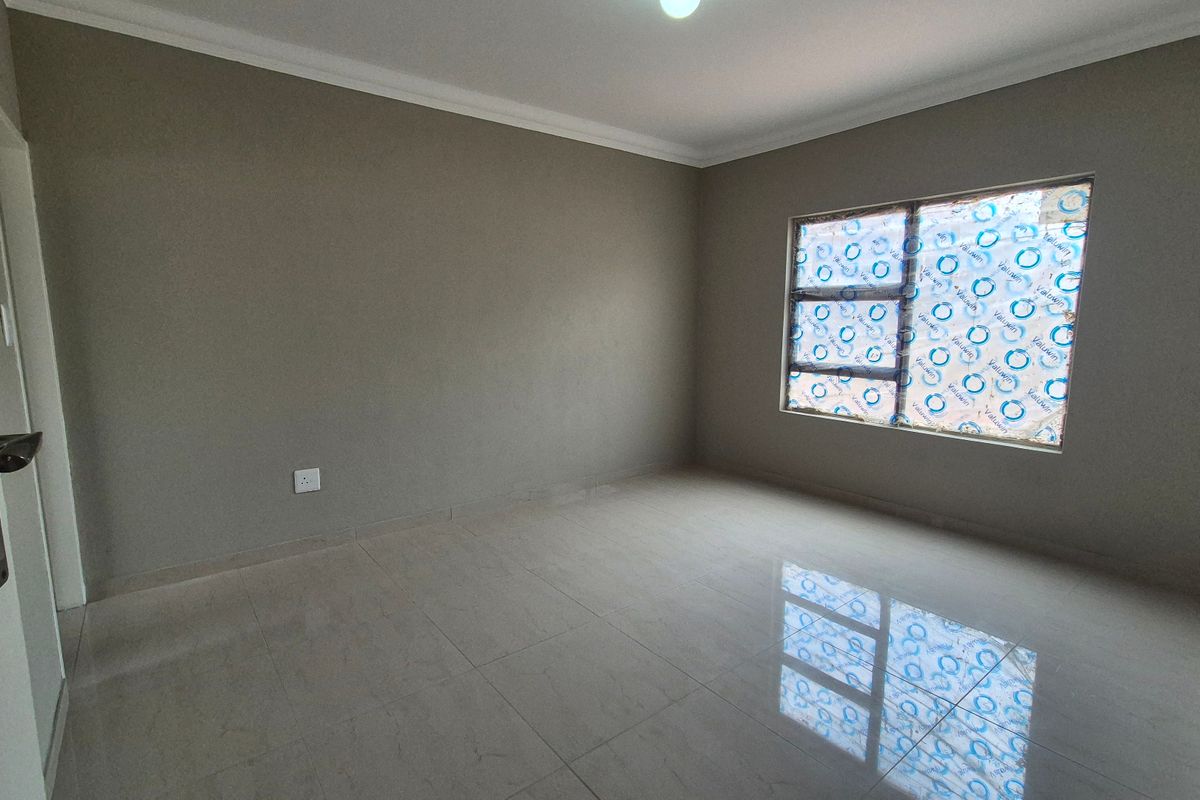A clean, empty bedroom featuring neutral wall paint, polished tiled flooring, and a large window with protective film still attached.