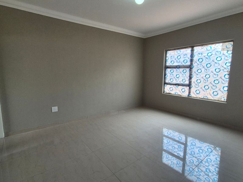 A clean, empty bedroom featuring neutral wall paint, polished tiled flooring, and a large window with protective film still attached.