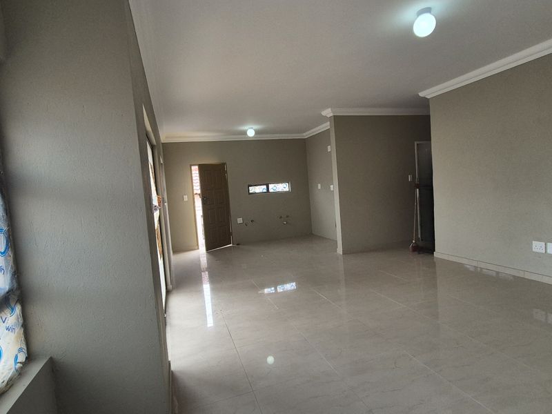 A spacious, empty open-plan living area featuring neutral wall tones, tiled flooring, and modern finishes, ready for personalization.